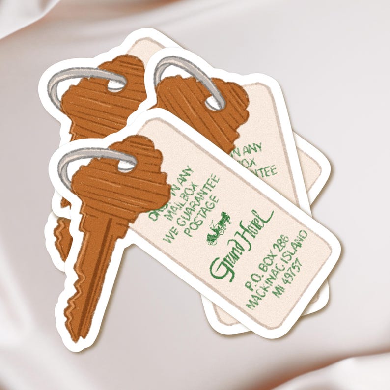 May include: A stack of stickers featuring vintage-style hotel key tags. The tags are cream-colored with brown keys and green text that reads "Grand Hotel, Mackinac Island, MI 49757". The tags also include the text "We Guarantee Postage".