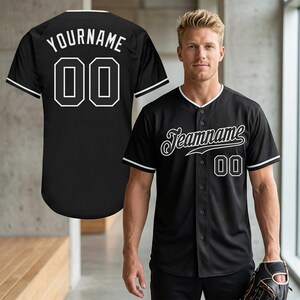 Pode incluir: Camisola de beisebol preta com acabamentos e botões brancos. A camisola apresenta o texto "Teamname" em fonte cursiva na frente e o número "00". A parte de trás da camisola exibe o texto "YOURNAME" e o número "00".
