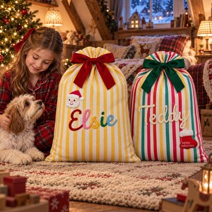以下が含まれることがあります： 巾着とリボンが付いた2つの大きな布製クリスマスギフトサック。1つは黄色と白のストライプで、サンタのアップリケとカラフルな刺繍で「Elsie」という名前が入っています。もう1つは赤、緑、白のストライプで「Teddy」という名前が入っています。