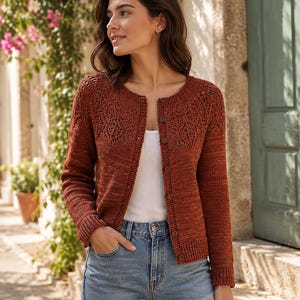 Könnte beinhalten: Eine rostfarbene Strickjacke mit Rundhalsausschnitt, langen Ärmeln und einer durchgehenden Knopfleiste. Der obere Brustbereich ist mit einem komplizierten Spitzenmuster versehen, während der Rest des Kleidungsstücks eine glatte Textur aufweist.