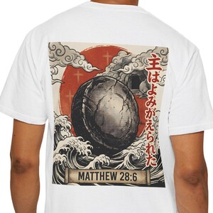 May include: White t-shirt featuring a Japanese-inspired graphic on the back. The design includes a large, dark sphere, a red sun, stylized waves, and text in both English and Japanese. The text "Matthew 28:6" is also present.