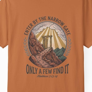 May include: Orange t-shirt with a graphic design featuring a path leading to a gate, with the text "ENTER BY THE NARROW GATE ONLY A FEW FIND IT" and the Bible verse Matthew 7:13-14.