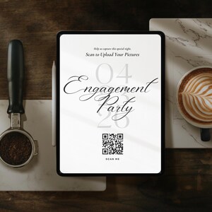 May include: An engagement party invitation displayed on a tablet, with the date and a QR code. A cup of latte art and a coffee machine portafilter are on marble tiles, set on a dark wood surface.