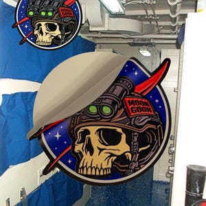 Könnte beinhalten: Runder Aufkleber mit einem Totenkopf, der einen Militärhelm mit Nachtsichtgeräten trägt. Der Aufkleber hat einen blauen Hintergrund mit weißen Sternen und den Worten "MOON GOON". Rote Akzente vervollständigen das Design.