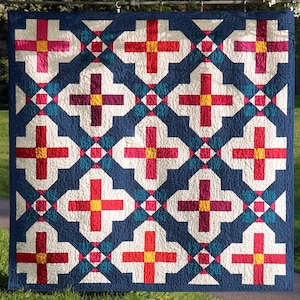May include: A quilt with a geometric pattern in shades of red, white, yellow, and blue. The quilt is made up of squares and crosses, and the background is a deep blue.