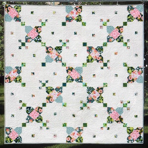 May include: A white quilt with a floral pattern in shades of pink, green, and blue. The quilt is made up of squares and is hanging on a clothesline.