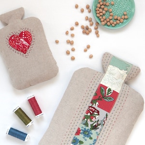 Può includere: Due bottiglie di acqua calda in tessuto fatte a mano con un design a cuore e patchwork floreale. Le bottiglie sono in lino naturale e presentano una varietà di colori, tra cui rosso, verde, blu e bianco. Le bottiglie sono riempite di ceci e sono perfette per fornire calore e comfort.