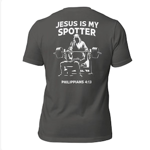 Może przedstawiać: Ciemnoszara koszulka z białą grafiką na plecach. Grafika zawiera napis "JESUS IS MY SPOTTER" nad ilustracją osoby podnoszącej ciężary. Poniżej ilustracji znajduje się napis "PHILIPPIANS 4:13".