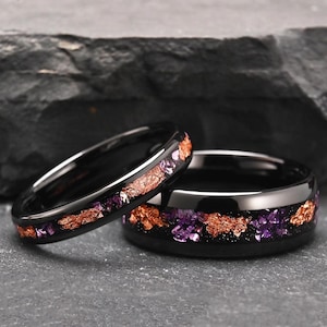 Peut inclure: Deux bagues noires avec une finition polie et une incrustation centrale de flocons de cuivre et d'améthyste violette broyée. Les bagues présentent un profil lisse et arrondi ainsi qu'une surface sombre et réfléchissante aux textures variées.