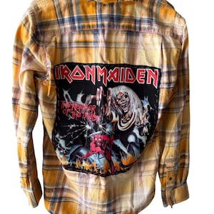 May include: Yellow plaid flannel shirt with an Iron Maiden patch on the back. The patch features the band's logo and artwork from "The Number of the Beast" album. The shirt has long sleeves and a button-down front.