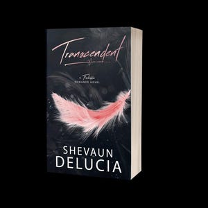 May include: A hardcover book titled "Transcendent" by Shevaun DeLucia. The cover features a pink feather against a dark background. The book is a Forbidden Romance Novel.