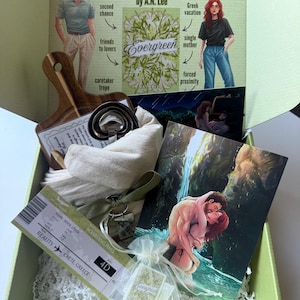 May include: A gift box containing a book titled Evergreen by A.N. Lee, a wooden serving board, a set of metal measuring cups, a beige cloth bag with a green ribbon, a boarding pass to Crete, Greece, and two romantic illustrations of a couple.
