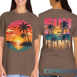 May include: Espresso-colored t-shirt featuring a sunset scene with palm trees and the text "SUN SEA SAND" on the back. The front design shows a sunset over the ocean with palm trees and birds. The shirt is a comfortable fit.