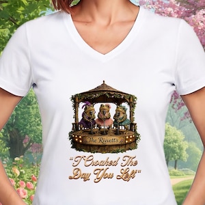 Puede incluir: Camiseta blanca con cuello en V con un diseño caprichoso de tres ranas músicas en un escenario. Las ranas visten trajes coloridos y están bajo una glorieta de madera. También se muestra el texto "The Rivett's" y "I Croaked The Day You Left".