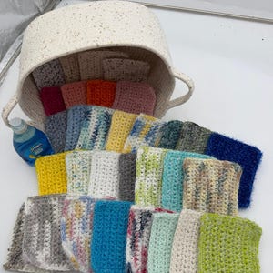 Peut inclure: Collection de débarbouillettes crochetées à la main, aux couleurs vives, dont le jaune, le bleu, le vert et le gris. Elles sont disposées devant un panier en osier, suggérant un thème d'articles ménagers ou de cuisine.
