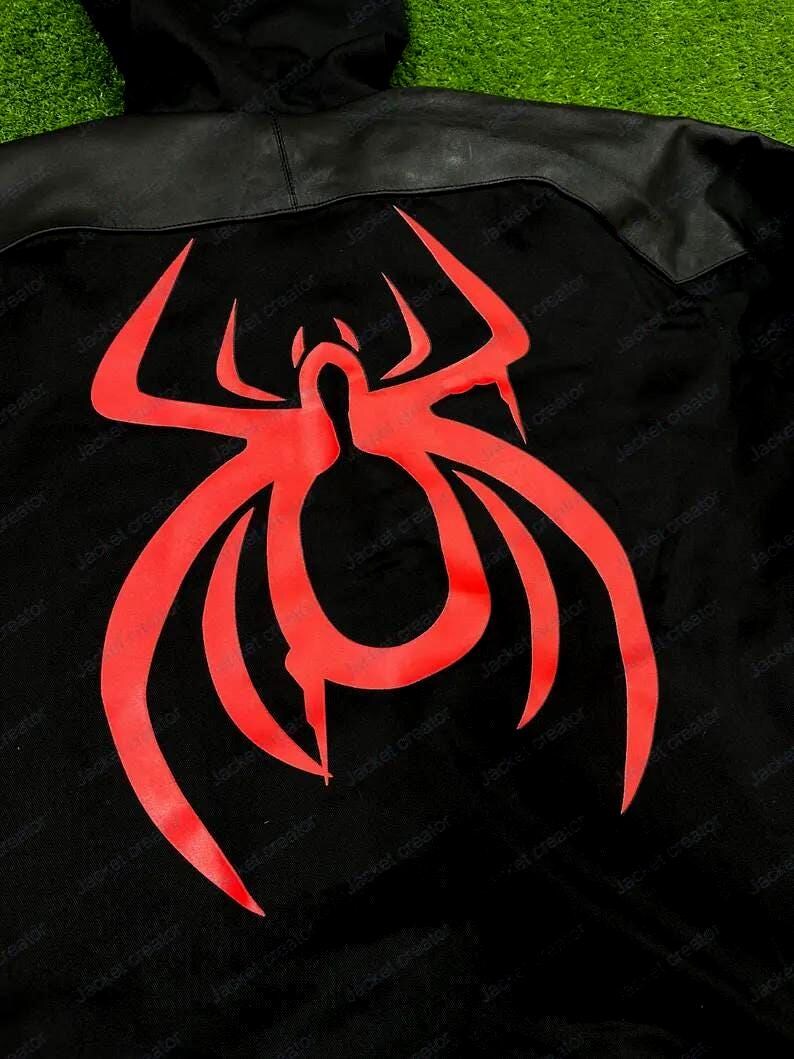 May include: Black jacket with a red spider emblem on the back. The jacket has a hood and a leather-like panel across the shoulders. The spider design is a bold, stylized graphic.
