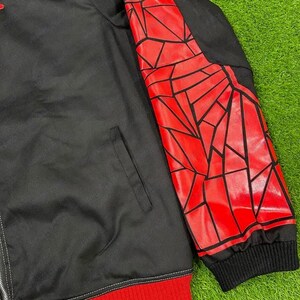 May include: Black jacket with a red geometric design on the right sleeve. The jacket has a black collar and a red ribbed hem and cuffs. A silver zipper runs down the front.