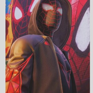 May include: A black and red Spider-Man costume with a hooded jacket. The mask has white eye lenses and a red web pattern. The jacket features red geometric designs on the sleeves and a zipper closure. A Spider-Man mural is in the background.