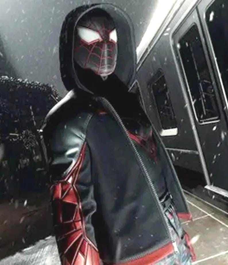 May include: A black hooded jacket with red and black accents, featuring a spider-themed design. The jacket has a zipper closure and is worn over a patterned shirt. The image is set against a snowy background.