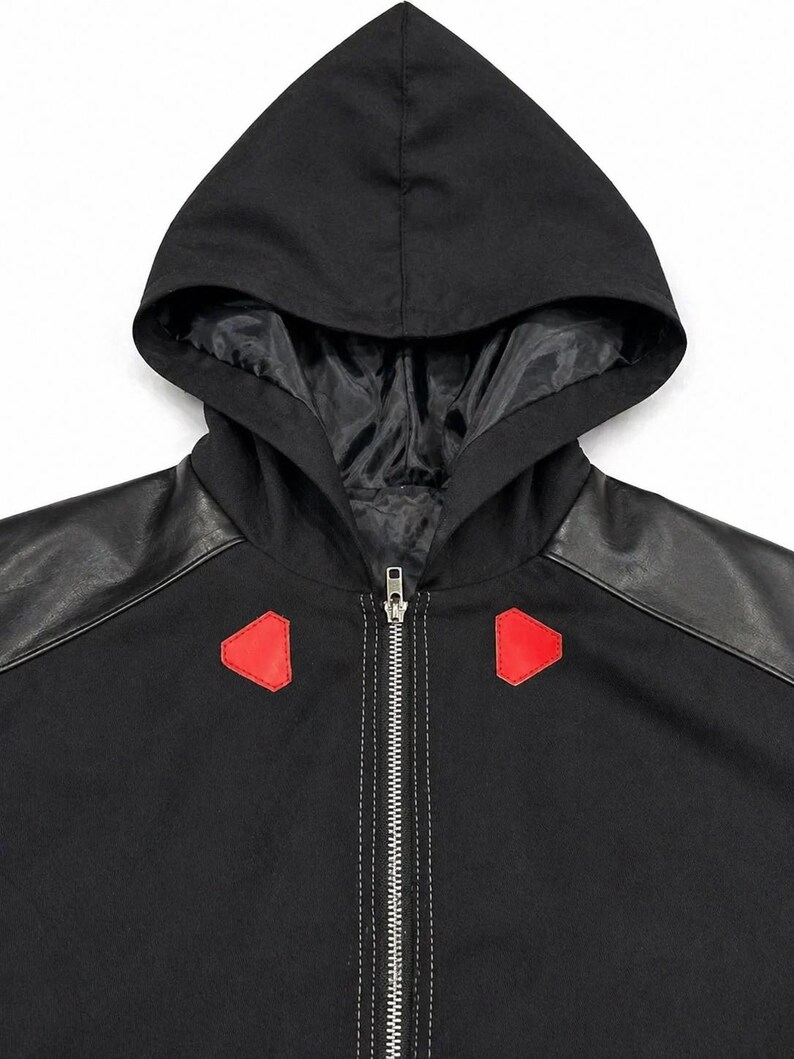 May include: Black hooded jacket with black faux leather shoulder panels and red geometric accents. The jacket features a full-length zipper and a black hood with a satin lining. The stitching is white.