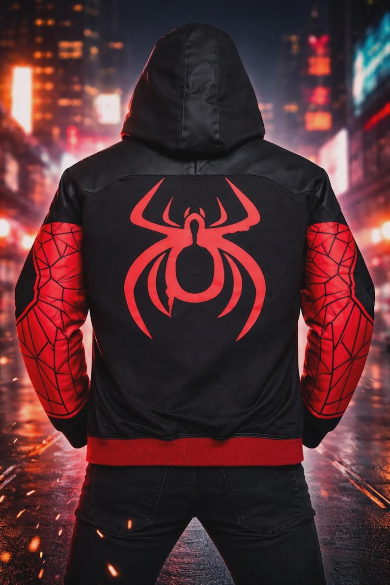 May include: Black bomber jacket with a red spider emblem on the back and red spiderweb-patterned sleeves. The jacket has a black hood and red trim at the waist and cuffs. The background is a blurred city scene.