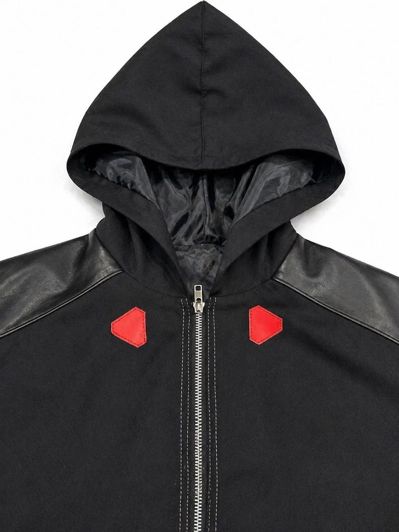 May include: Black hooded jacket with a full-length zipper and red accents. The jacket features black faux leather shoulder panels and a black hood with a satin lining. The hood is attached to the jacket's collar.