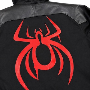 May include: Black hooded jacket with a red spider graphic on the back. The jacket features a black leather panel across the shoulders and hood. The spider design is a bold, stylized illustration.