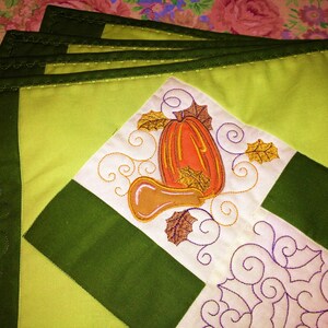 May include: Set of four green and yellow fabric placemats with an embroidered design of gourds and leaves.
