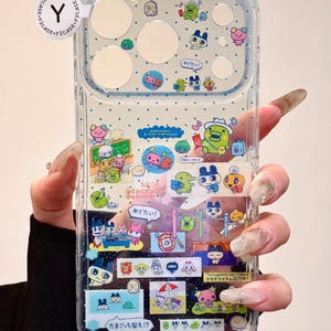 May include: Clear phone case with a cartoon design featuring various characters and Japanese text. The case has a glittery appearance and includes images of cute creatures and text bubbles.