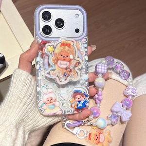 May include: Clear phone case with a lavender border, featuring cartoon characters and a beaded strap. The case has a teddy bear with a star, a bunny, and a sailor bear. The strap includes purple beads, bows, and a dog charm.