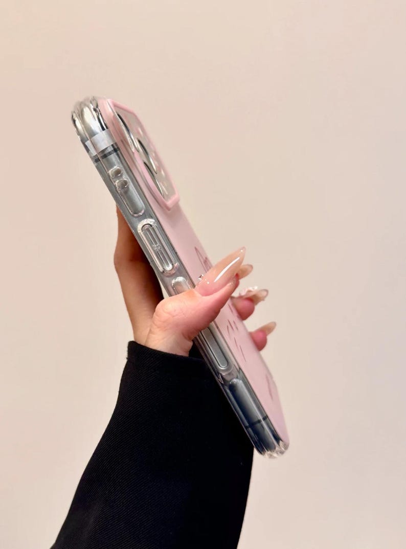 May include: A clear phone case with a pink interior and a silver border. The case is held at an angle, showcasing its design. The phone case is a protective accessory for smartphones.