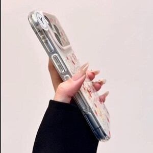May include: Clear phone case with a floral design featuring red and yellow flowers. The case has a white border and a clear back, offering protection while showcasing the phone's design. A white sticker with a black "Y" is on the top left corner.