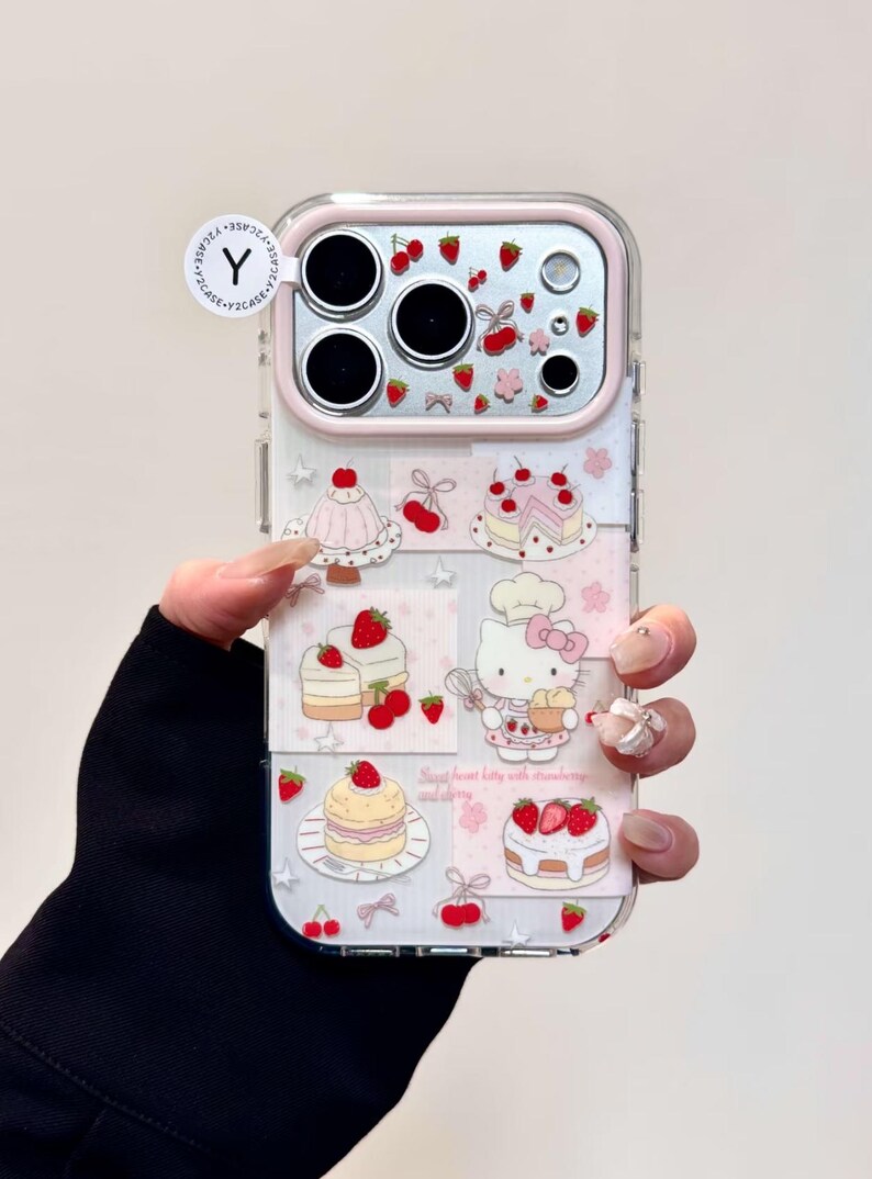 May include: Clear phone case with a pink border featuring a design of cakes, strawberries, and a cartoon cat. The case has a clear back and a pink camera border. The text "Sweet heart kitty with strawberry and cherry" is visible.