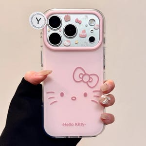 May include: Pink phone case featuring a Hello Kitty design. The case has a clear border and includes a bow, face, and the text "Hello Kitty". The camera area has decorative elements.