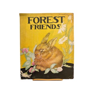 May include: Vintage book cover titled "FOREST FRIENDS" featuring a brown rabbit surrounded by white daisies, pink clover, and green leaves against a yellow background. The book is propped up on a wooden stand.