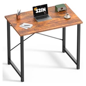 May include: A rectangular desk with a brown wood-grain finish and black metal legs. A laptop with "32IN" on the screen, a small green radio, and a cup of coffee sit on the desk. A pen holder and notepad are also visible.