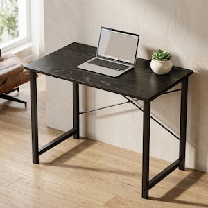 May include: A rectangular black desk with a wood grain finish and a black metal frame featuring cross-bracing supports. A silver laptop is open on the desk surface, and a small green succulent plant in a white pot sits in the corner.