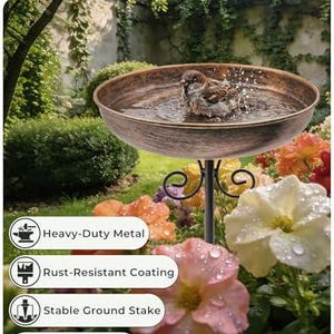 May include: A round, copper-toned metal bird bath basin with a textured finish, supported by a black metal stand with scrollwork details. A small brown bird is splashing in the water inside the basin. The text "Built for Outdoors" is visible.
