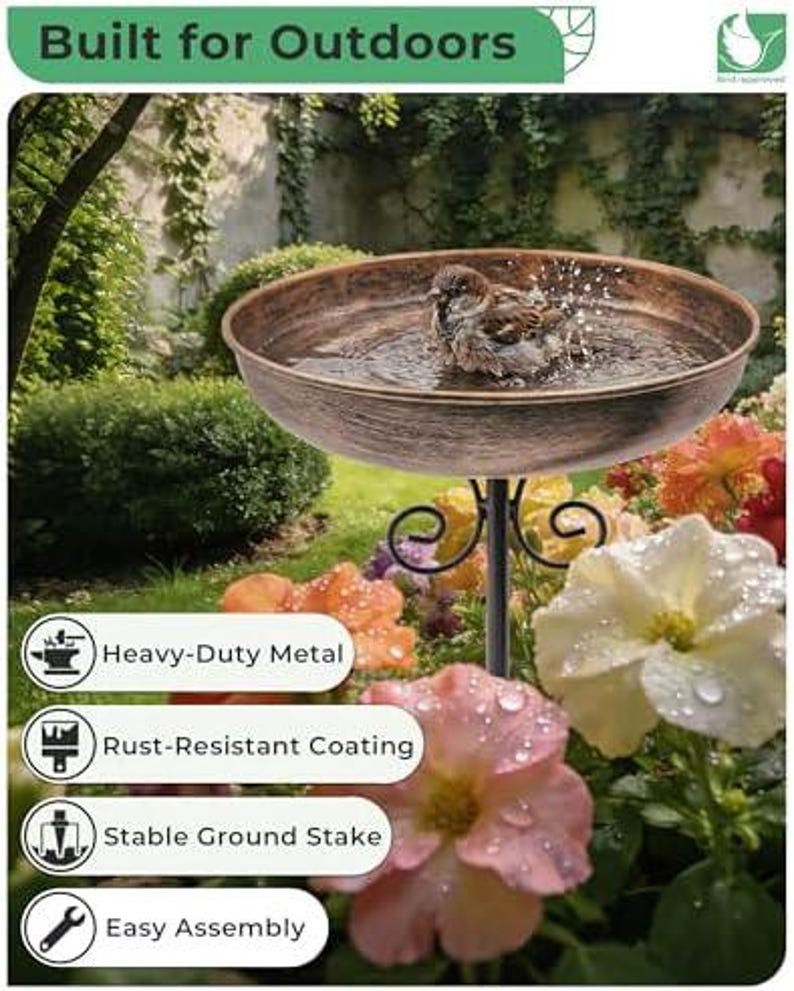 May include: A round, copper-toned metal bird bath basin with a textured finish, supported by a black metal stand with scrollwork details. A small brown bird is splashing in the water inside the basin. The text "Built for Outdoors" is visible.