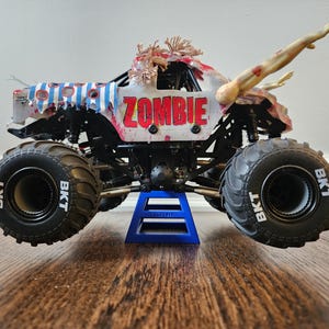 May include: A toy monster truck with the word "ZOMBIE" in red letters on the side. The truck has large black tyres with "BKT" printed on them. It is decorated with zombie-themed details, including arms reaching out.