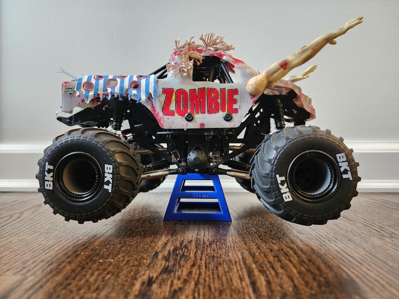 May include: A toy monster truck with the word "ZOMBIE" in red letters on the side. The truck has large black tyres with "BKT" printed on them. It is decorated with zombie-themed details, including arms reaching out.