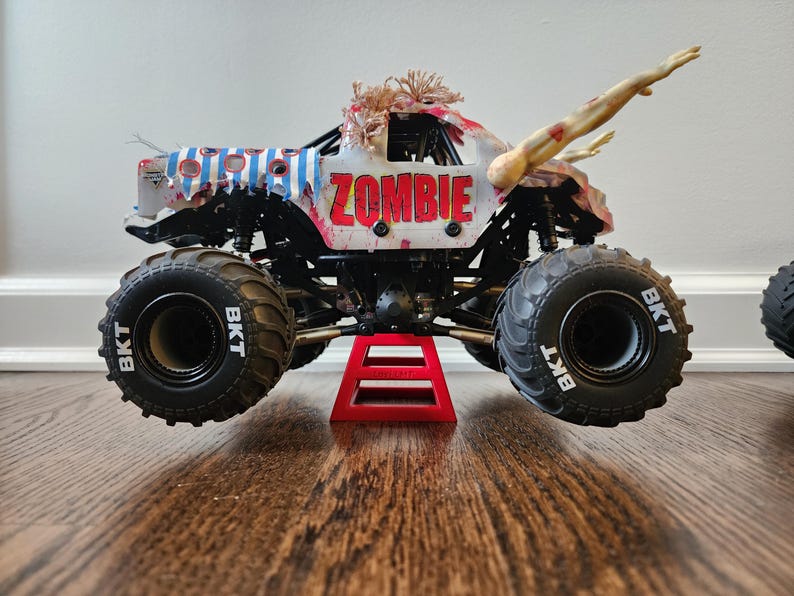 May include: A toy monster truck, white with blue stripes and the word "ZOMBIE" in red. It has large black tyres with "BKT" on them. The truck is supported by a red stand and features a zombie arm.