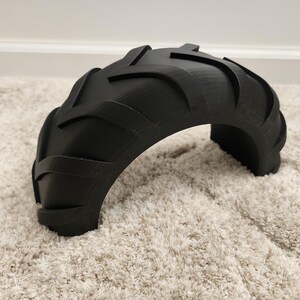 以下が含まれることがあります： 黒い半円形のオブジェクトで、タイヤのトレッドに似ています。 オブジェクトは、隆起したテクスチャパターンを持つ湾曲した形状をしています。 このアイテムは、おそらく装飾品またはより大きなデザインの一部です。