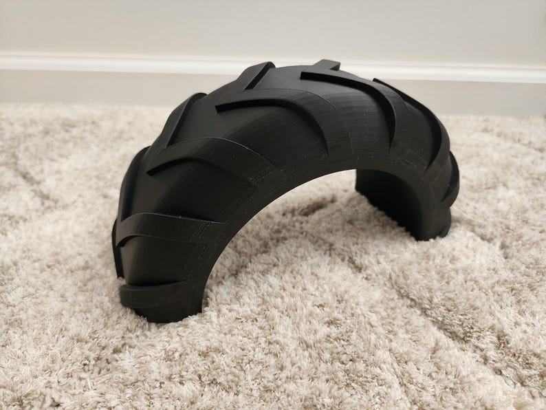 以下が含まれることがあります： 黒い半円形のオブジェクトで、タイヤのトレッドに似ています。 オブジェクトは、隆起したテクスチャパターンを持つ湾曲した形状をしています。 このアイテムは、おそらく装飾品またはより大きなデザインの一部です。