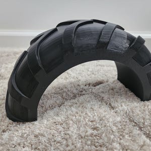 以下が含まれることがあります： タイヤのようなトレッドパターンを持つ黒い半円形オブジェクト。オブジェクトは固体材料でできており、湾曲した形状をしています。トレッドデザインは、隆起した長方形のブロックと湾曲した溝を備え、テクスチャード加工された外観になっています。
