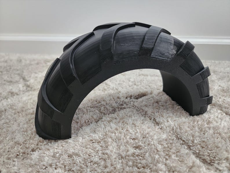 以下が含まれることがあります： タイヤのようなトレッドパターンを持つ黒い半円形オブジェクト。オブジェクトは固体材料でできており、湾曲した形状をしています。トレッドデザインは、隆起した長方形のブロックと湾曲した溝を備え、テクスチャード加工された外観になっています。