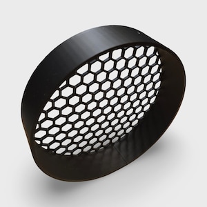 May include: A black, circular object with a honeycomb pattern. The object has a thick, rounded rim and a series of hexagonal openings in the center. The object is likely a decorative or functional element.