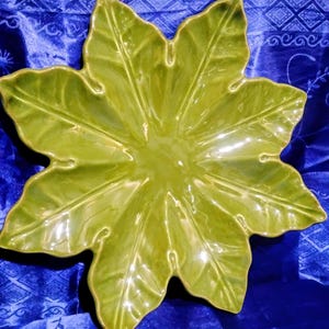May include: A glossy, lime green ceramic serving dish shaped like a stylized leaf. The dish has a central depression and radiating veins, with a smooth, reflective surface. The leaf-shaped dish is a decorative piece.