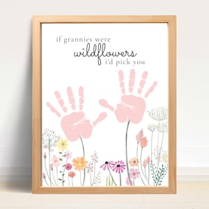 Könnte beinhalten: Ein gerahmter Druck mit dem Text "if grannies were wildflowers I'd pick you". Das Kunstwerk zeigt zwei rosa Handabdrücke über einer Aquarellillustration von bunten Wildblumen. Der Rahmen ist aus hellem Holz.