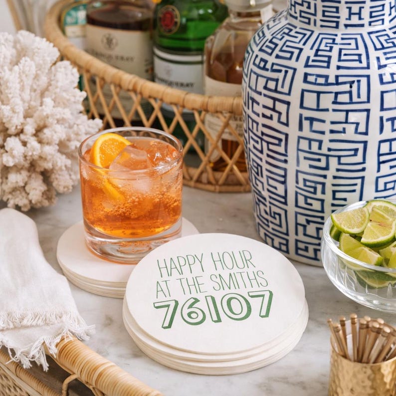 K&ouml;nnte beinhalten: Ein Stapel runder, cremefarbener Untersetzer mit dem gr&uuml;nen Text "HAPPY HOUR AT THE SMITHS 76107". Ein Cocktail mit einer Orangenscheibe steht auf einem Untersetzer. Weitere Artikel sind eine Vase, Limetten und Barzubeh&ouml;r.